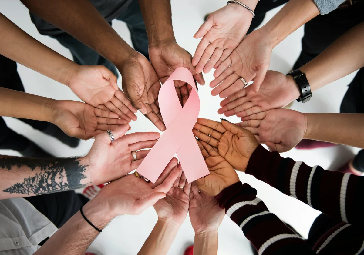 Women supporting each other with a pink ribbon for breat cancer at the centre of their hands 